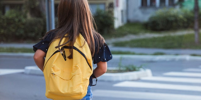 Young student with yellow book bag crosses the street.