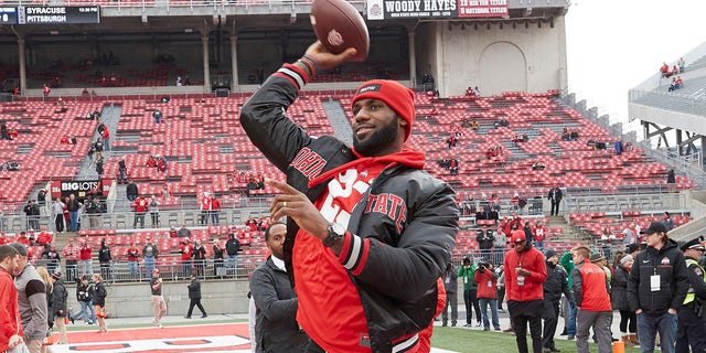 Cleveland Cavalier LeBron James passes on the field with teammate J.R. Smith before an Ohio State-Michigan game at Ohio Stadium in Columbus, Ohio, Nov. 26, 2016.  