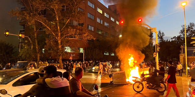 A fire releases a large amount of smoke with protesters gathered around it