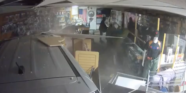 Screenshot of video showing a car that crashed through CC Coins Jewelry and Loan in Michigan and robbers ransacking the shop of guns.