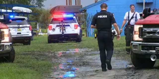 Un oficial de policía de Orlando camina hacia un bombero mientras los socorristas buscan a un remero que desapareció luego de un rayo en el lago Fairview.