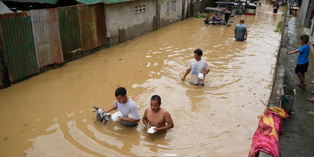 Residents carrying food packs wade along a flooded street from Typhoon Noru in San Miguel town, Bulacan province, Philippines, Monday, Sept. 26, 2022.