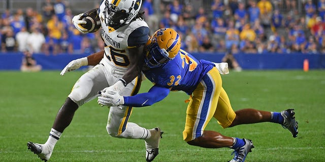 Justin Johnson Jr. #26 of the West Virginia Mountaineers is wrapped up for a tackle by Shayne Simon #32 of the Pittsburgh Panthers in the second quarter during the game at Acrisure Stadium on September 1, 2022 in Pittsburgh, Pennsylvania.