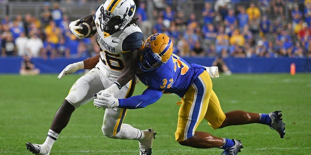 Justin Johnson Jr. #26 of the West Virginia Mountaineers is wrapped up for a tackle by Shayne Simon #32 of the Pittsburgh Panthers in the second quarter during the game at Acrisure Stadium on September 1, 2022 in Pittsburgh, Pennsylvania.
