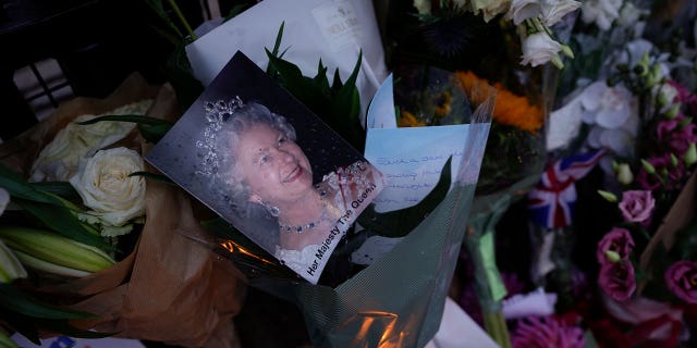 A photo of Queen Elizabeth along with messages, flowers and candles are seen at the gates of Buckingham Palace in London on Sept. 9, 2022.