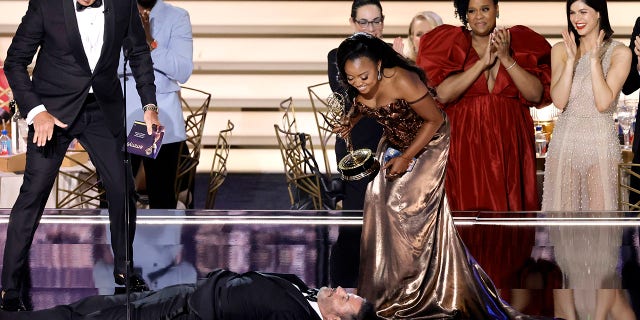 Quinta Brunson (R) accepts Outstanding Writing for a Comedy Series for "Abbott Elementary" from Will Arnett (L) while Jimmy Kimmel lies onstage during the 74th Primetime Emmys at Microsoft Theater on Sept. 12, 2022 in Los Angeles. 