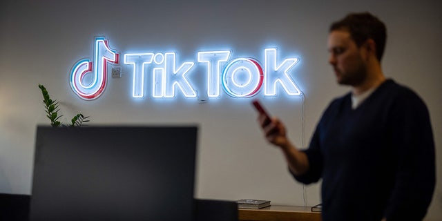 An employee looks at his mobile phone as he walks past the logo of the video-focused social networking service TikTok, at the TikTok U.K. offices, in London, on Feb. 9, 2022.