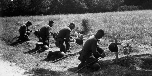 August 1944: American soldiers kneel in homage at the graves of their dead comrades near Sainte Mere Eglise. 