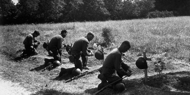 August 1944: American soldiers kneel in homage at the graves of their dead comrades near Sainte Mere Eglise.