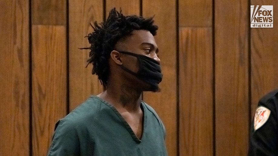 Ezekiel Kelly stands in court in green prison jumpsuit and black coronavirus mask
