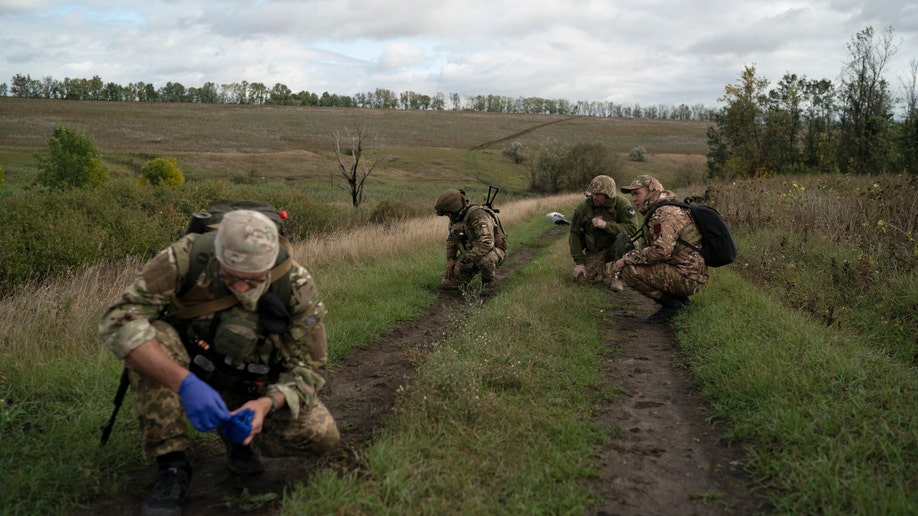 Ukrainian national guard servicemen crouch as a de-miner checks if a body of a Ukrainian soldier is booby-trapped