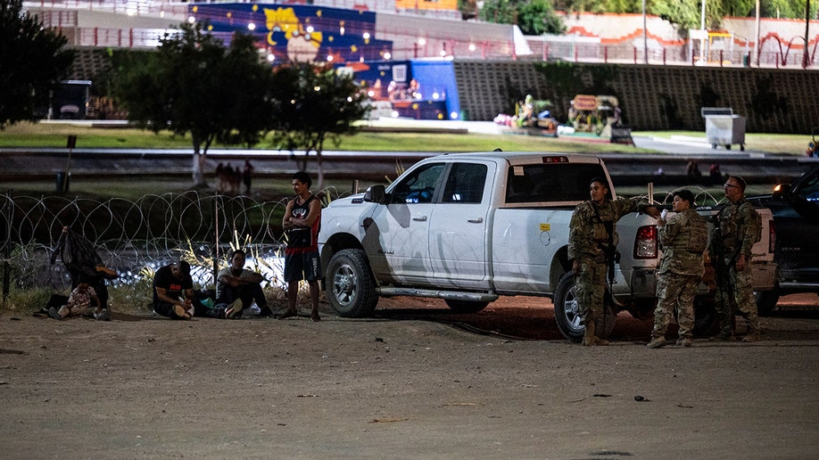 Migrants sitting by a CBP truck