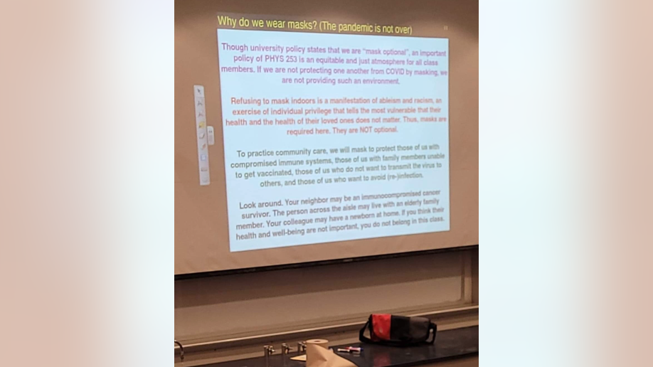 Photo shows a projector screen from Northern Illinois University saying masks are mandatory in class and not masking indoors is a "manifestation" of racism 