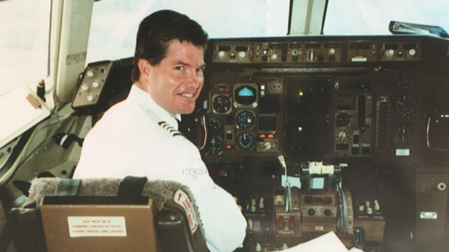 Photo shows pilot Chic Burlingame sitting in an American Airlines cockpit while smiling for the camera