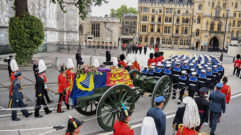 Queen Elizabeth's coffin laden with a flag is carried on a carriage and surrounded by guards in red uniforms