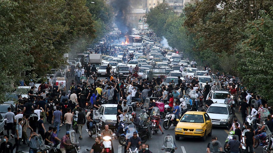 An overheard shot in Tehran showing a pile up cars with smoke rising in the background and protesters gathered at the forefront of the scene