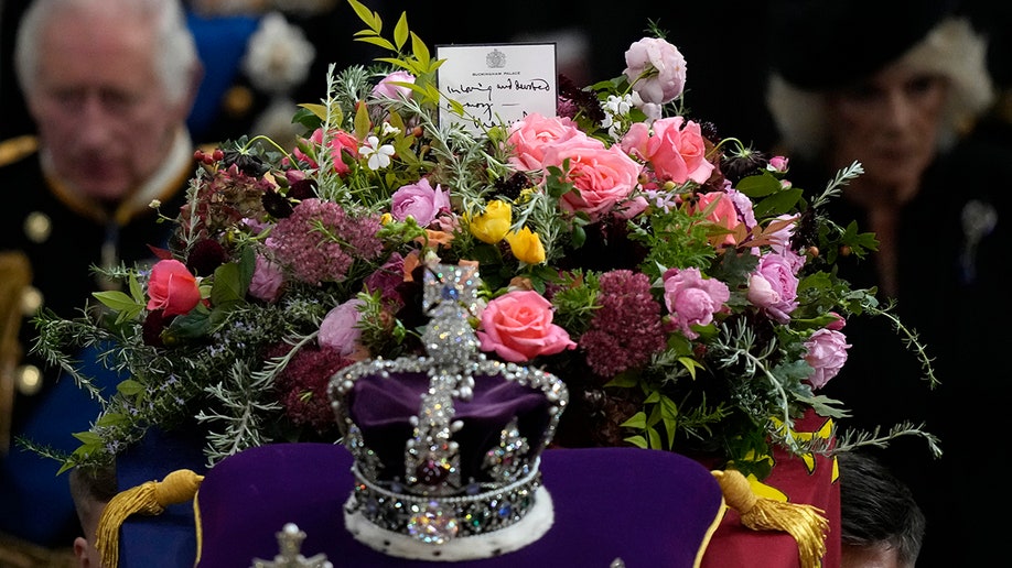 Purple velvet crown is laid upon a purple velvet cushion accompanied by flowers and a note from King Charles on Queen Elizabeth's coffin.