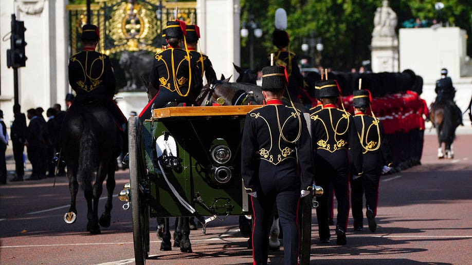 Artillery members in black uniforms walk alongside a carriage