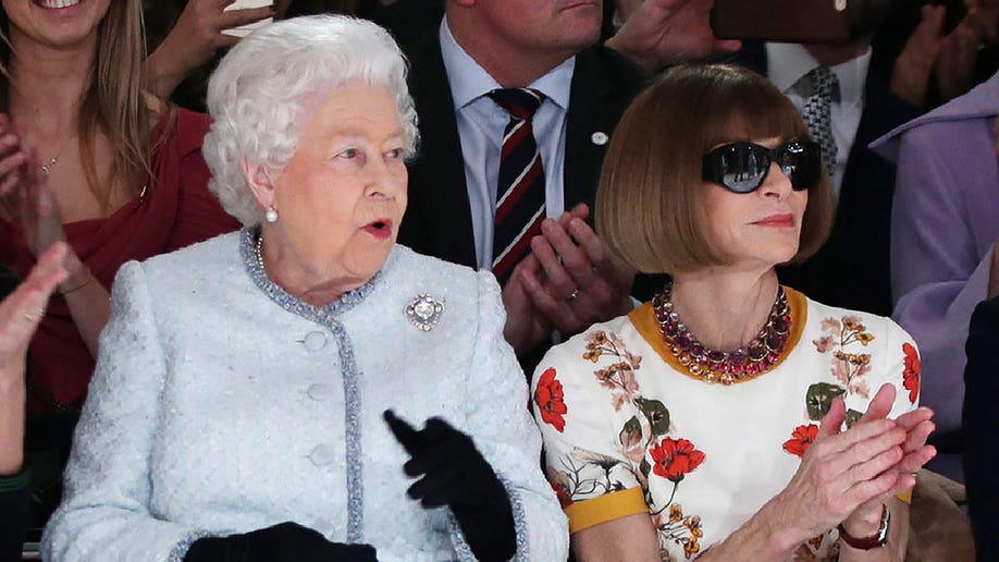 Queen Elizabeth has a surprised expression on her face while sitting next to Anna Wintour during a show