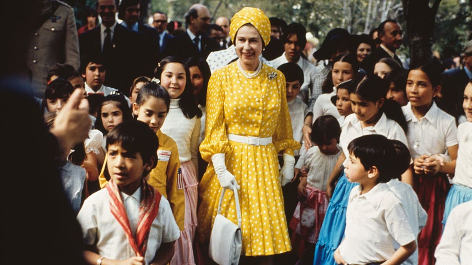 Queen Elizabeth wears a yellow polka dot dress while surrounded by school children in uniform