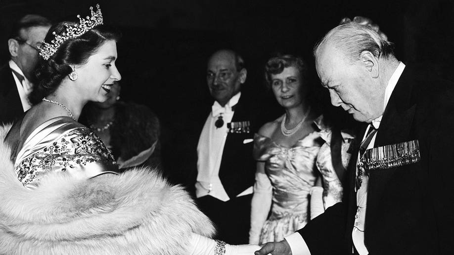 Queen Elizabeth wears furs and crown while shaking hands with Winston Churchill