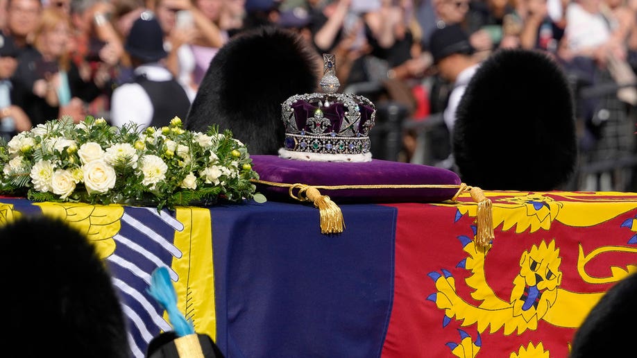Queen Elizabeth's coffin has flowers laid on top of it and a purple velvet crown on a cushion