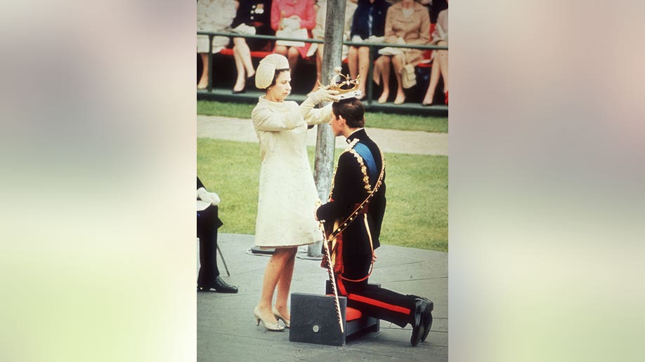 Queen Elizabeth wears a yellow dress while placing a crown on her son, Charles', head during an outside ceremony