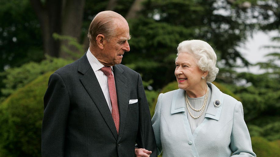 Queen Elizabeth and Prince Philip look at eachother for a portrait photo while standing outside