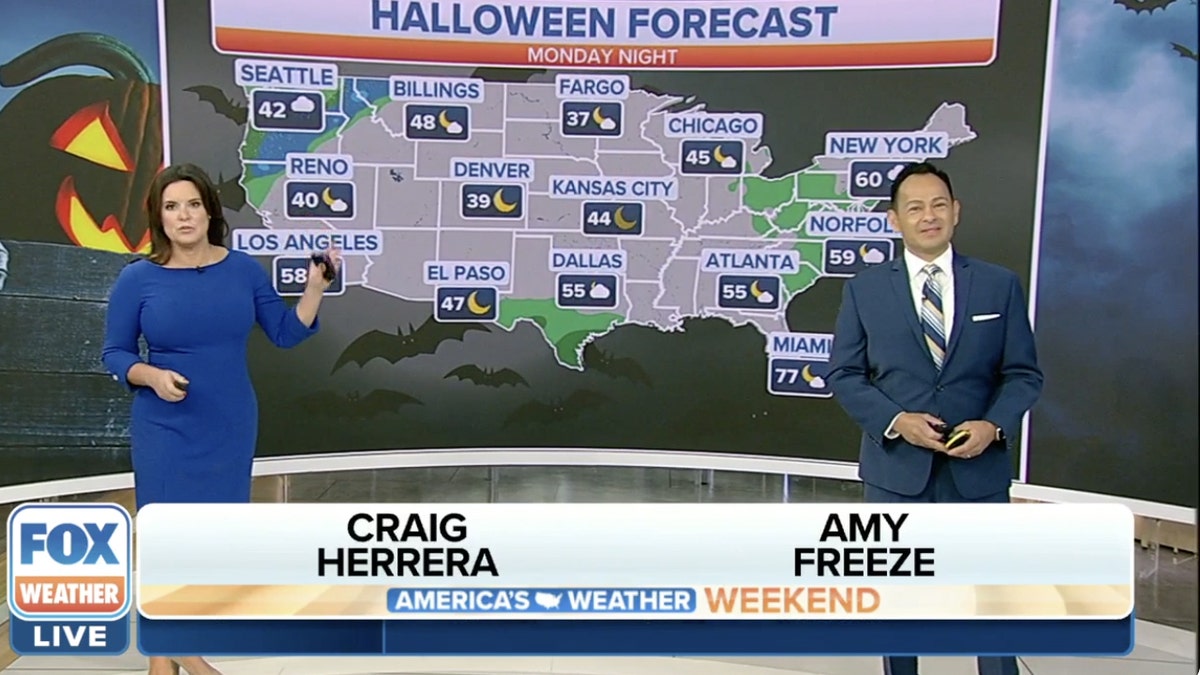 Two weather anchors standing in front of a map showing a halloween forecast