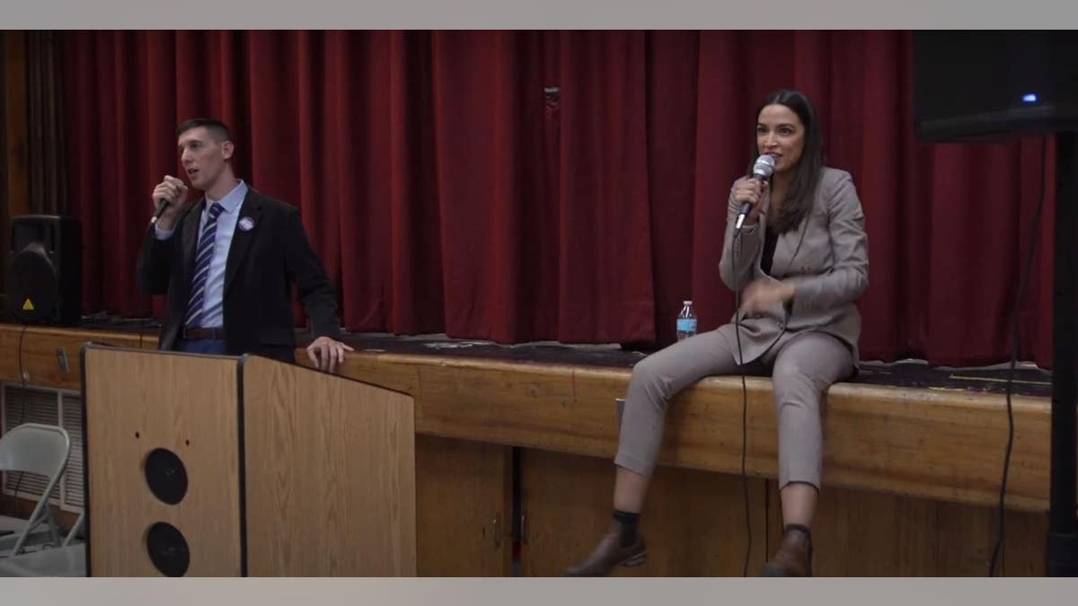 Alexandria Ocasio-Cortez sits on a stage.