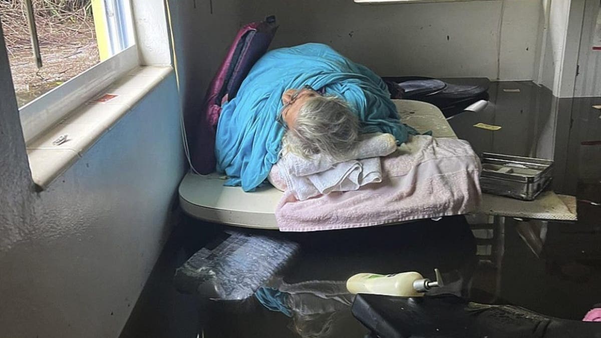 Johnny Lauder's mother, Karen Lauder, 86, lies just above the water line on a table, wrapped in sheets to keep warm after water flooded her home, in Naples, Fla., Wednesday, Sept. 28, 2022, following Hurricane Ian.