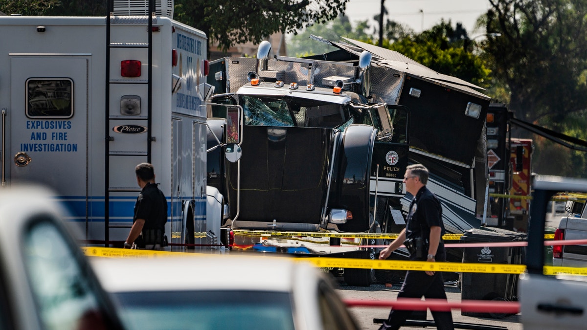 Officers walk past the remains of an armored trailor