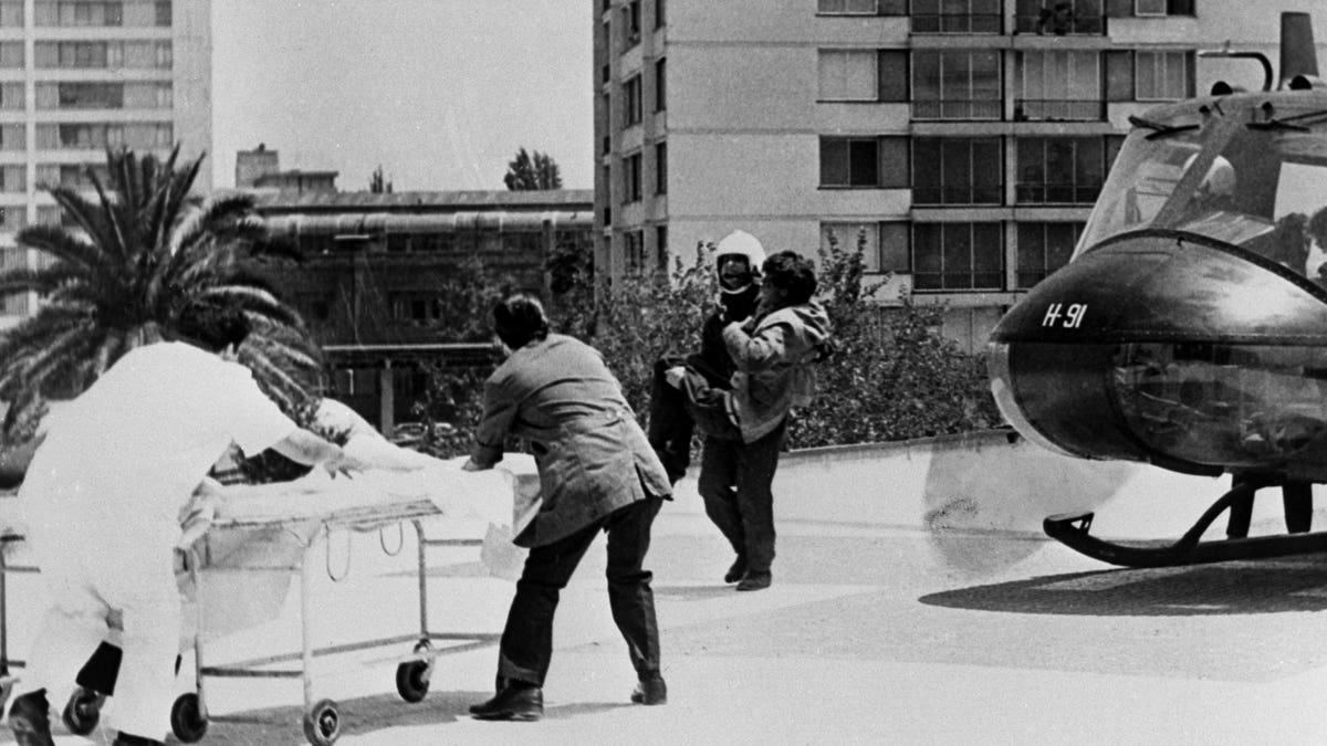 Helicopter on the right with a man being carried to a stretcher at the Santiago Central First Aid Station