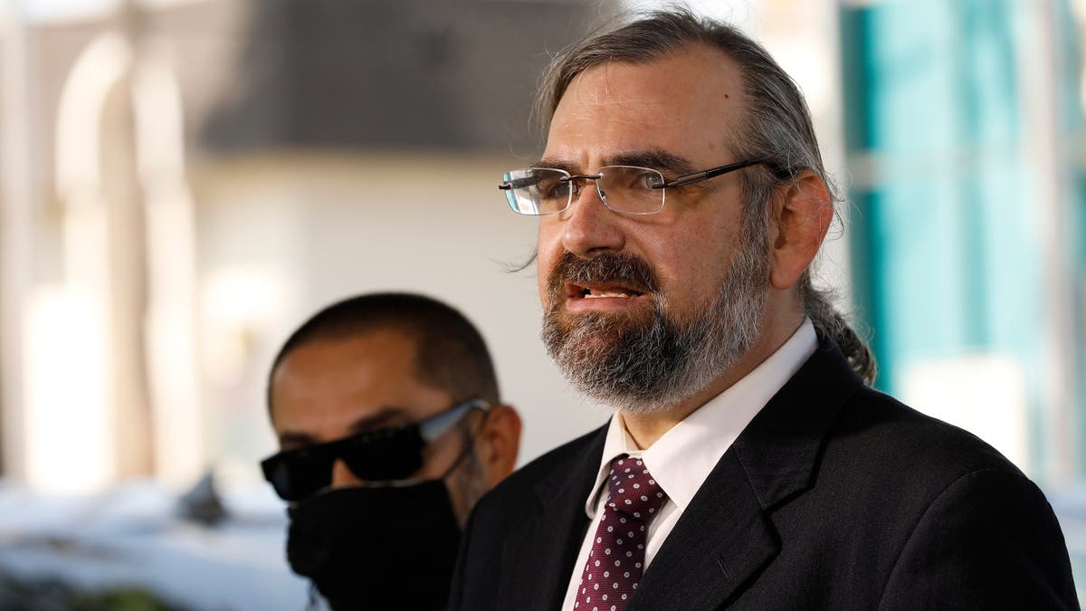 Attorney Robert Frommer wearing a suit and glasses, speaks to reporters