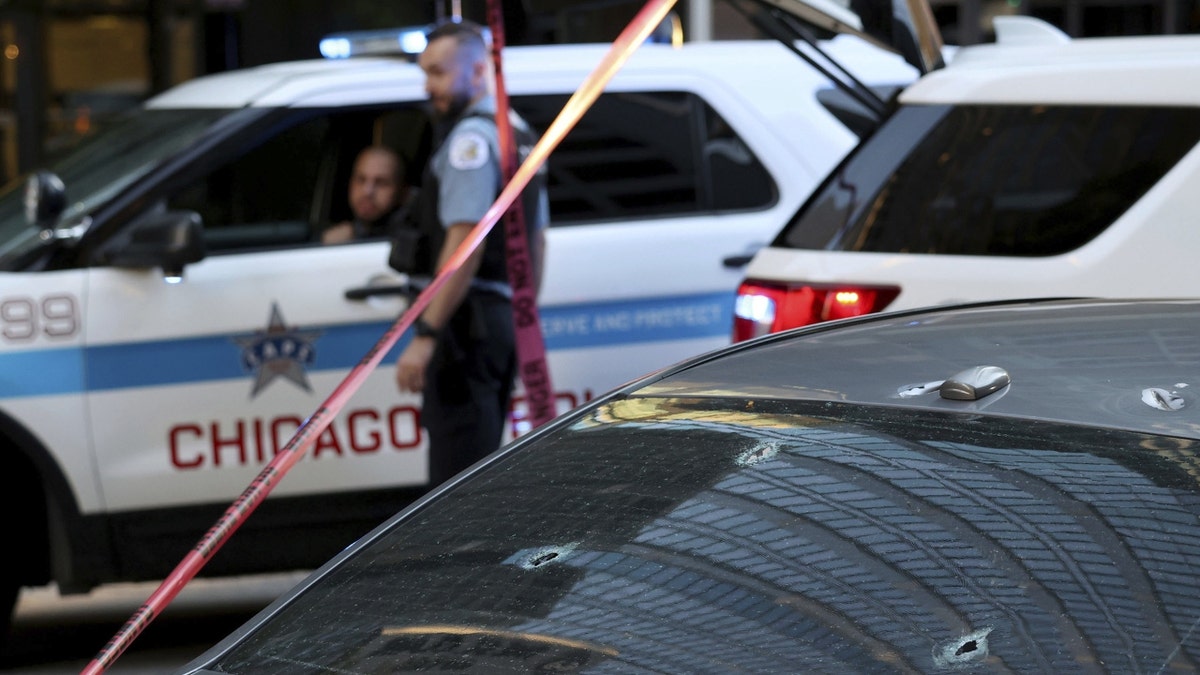 A Chicago cop stands next to a bullet-ridden car