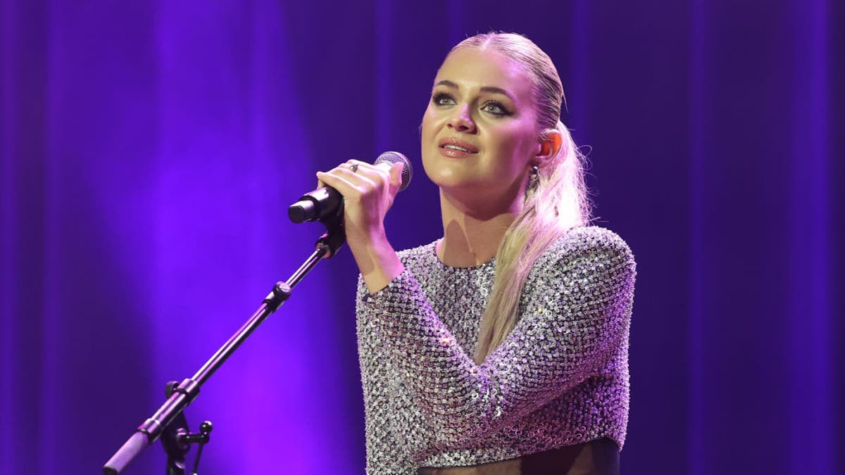 Kelsea Ballerini holds a microphone on a stand at the NSAI 2022 Nashville Songwriter Awards