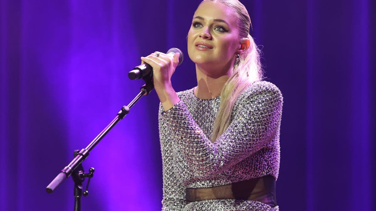 Kelsea Ballerini holds a microphone on a stand at the NSAI 2022 Nashville Songwriter Awards