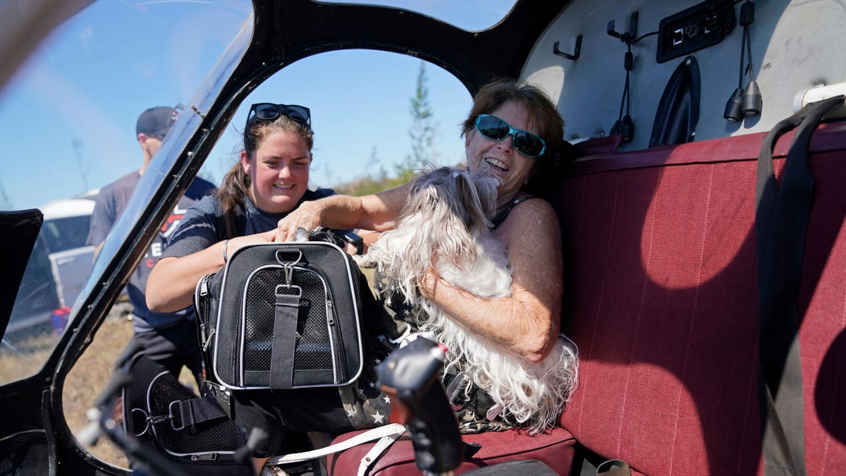Woman in helicopter with a dog in her lap and another woman helping her get in
