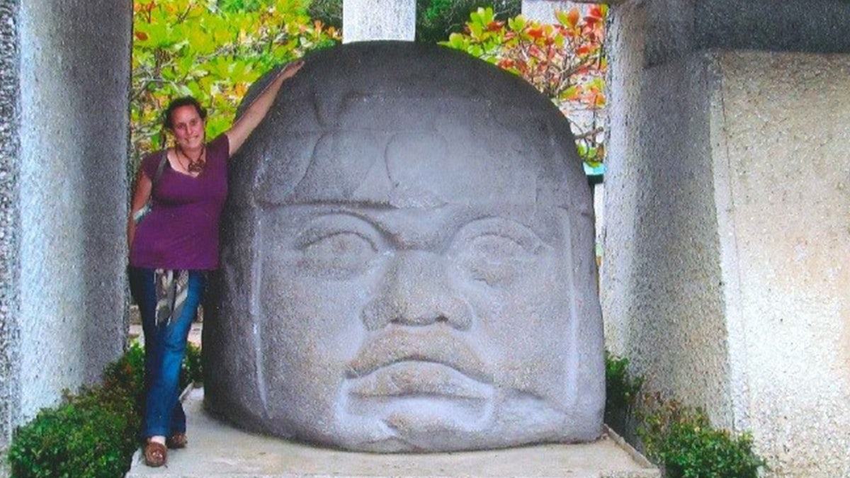 Leigh Brantley standing beside a large Mayan sculpture
