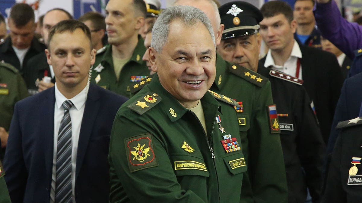 Sergei Shoigu smiles as he stands in front of crowd of military