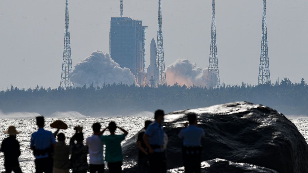 Onlookers sillhouettes as they watch space module launch from afar