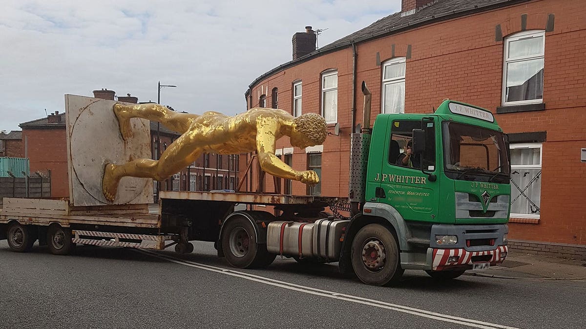 The golden statue lays face down on a truck bed as it is towe away