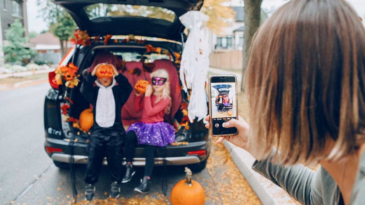 Children celebrating trunk-or-treat while mom records