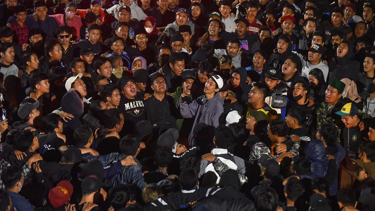 Soccer fans gather in crowd, crying and chanting, during vigil for soccer match victims