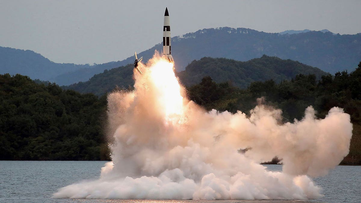 A missile is launched over a body of water with smoke jetting out 