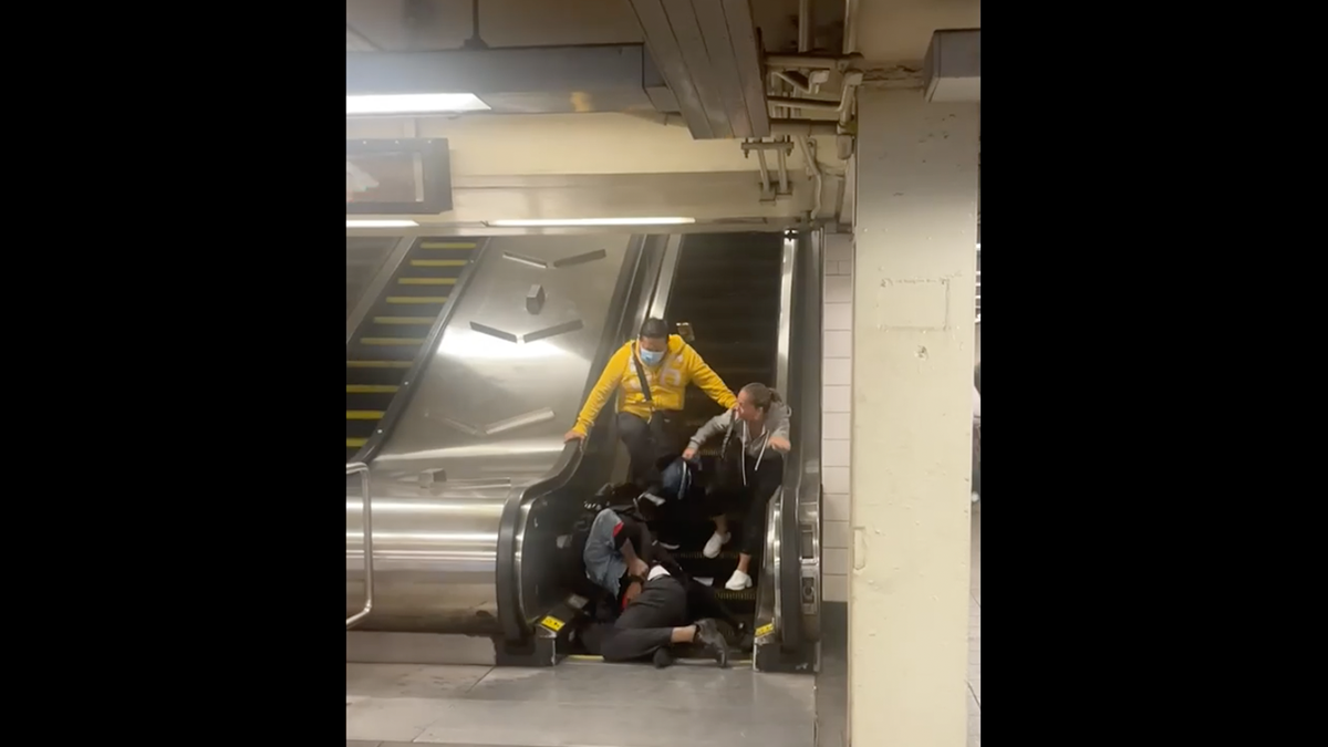 Screen shot shows four people at bottom of escalator after two people who were fighting fell