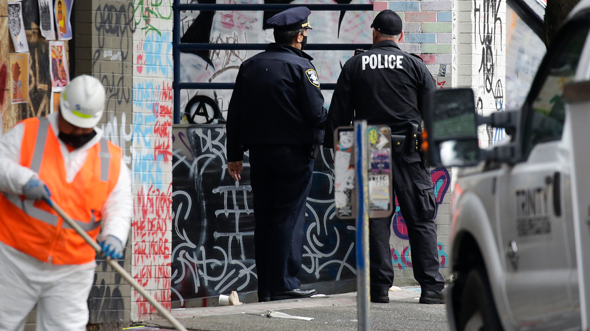 Two Seattle police officers seen in a photo while worker cleans up area of city in 2020