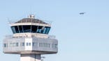 Air traffic control tower at Flesland Airport with a small propeller plane flying in the background