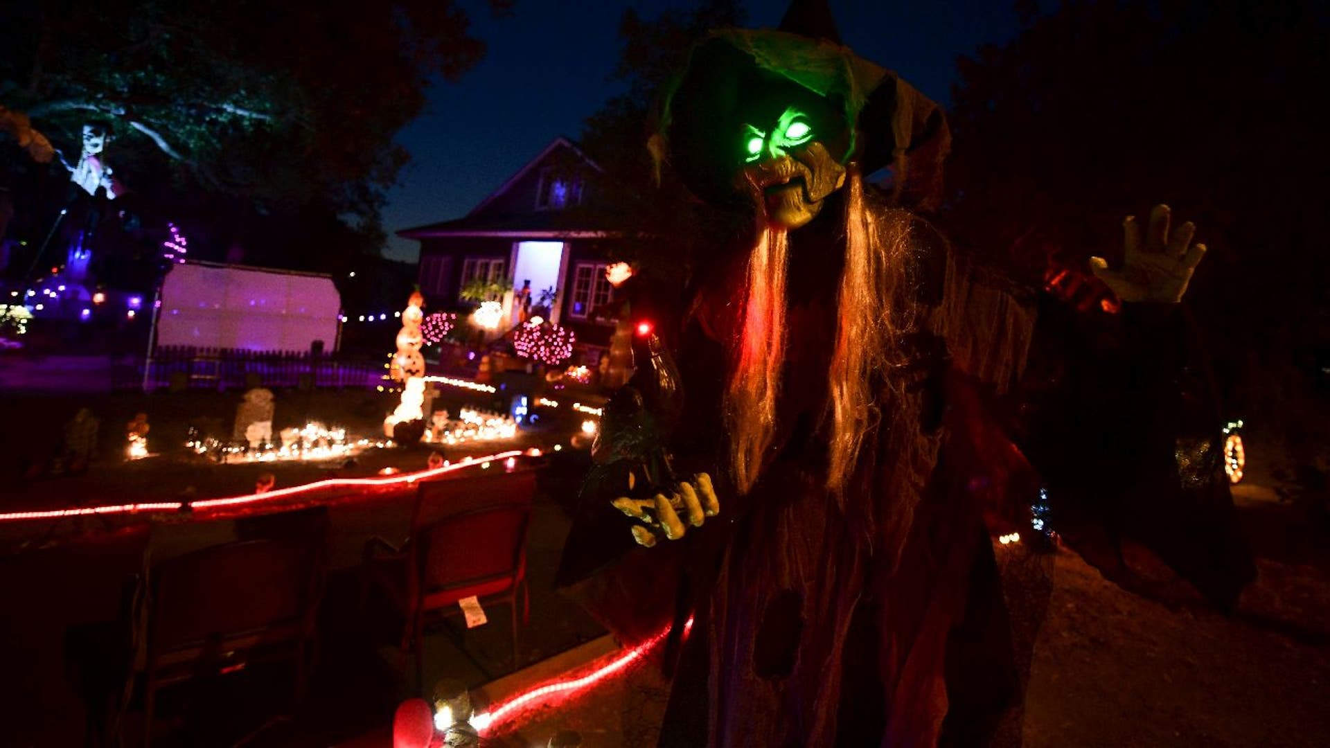 Life-size witch figure with glowing green eyes in a decorated yard