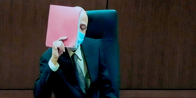Darrell Brooks shields his face with a folder during jury selection as he appears via video from an adjacent courtroom due to his continuous interruptions Oct. 3.